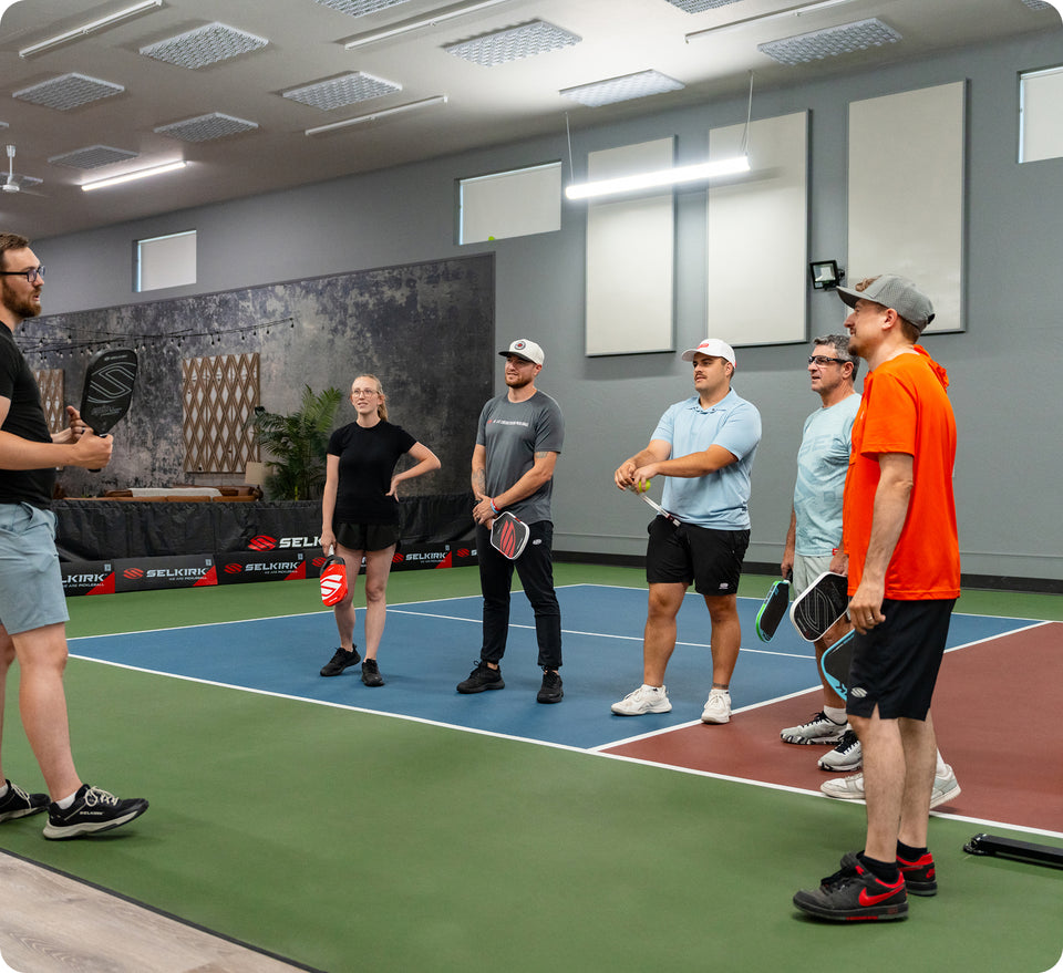 Indoor group pickleball lesson at Selkirk, coach instructing five adults on court during a corporate team event.