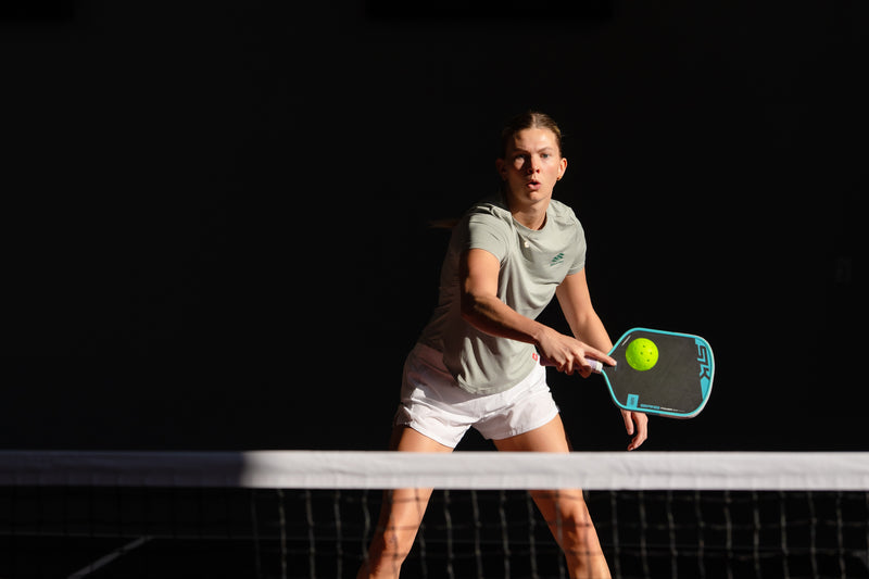 Person playing pickleball on a dark court