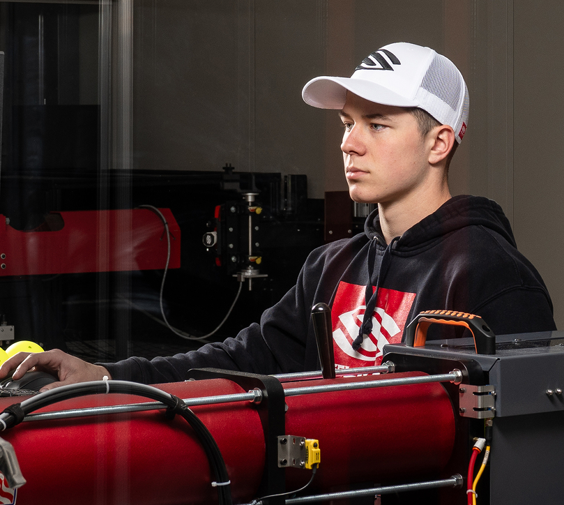 Selkirk Sport engineer operating high-precision manufacturing equipment for pickleball paddle production, wearing branded apparel and cap in a controlled lab environment.