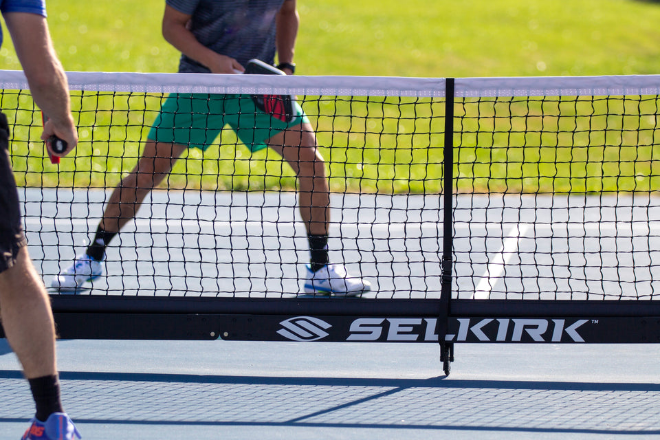 Pickleball players at the net, SELKIRK TM logo on the net bumper