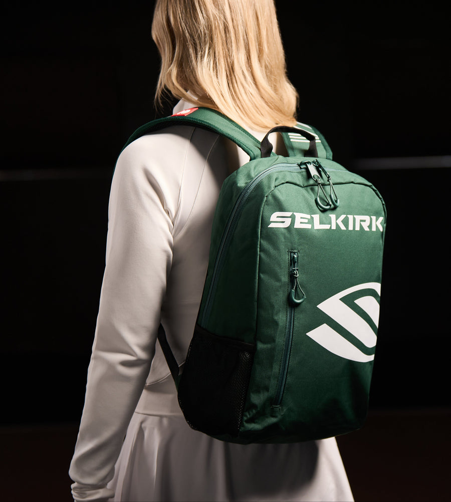 A person wearing a green SELKIRK backpack, showcasing its design.