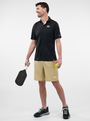 Man holding a pickleball paddle and ball, wearing a black polo and tan shorts, smiling and looking left
