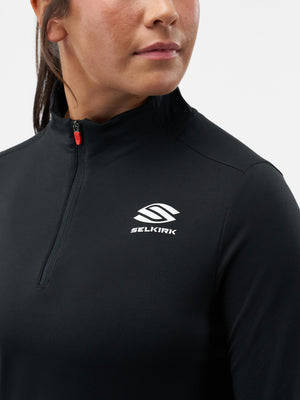 Woman wearing black quarter-zip athletic top with white SELKIRK logo on chest and red zipper pull, cropped at chin