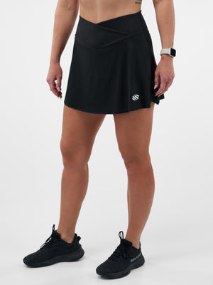 Women's black athletic skort with crossover waistband and small logo, shown on model from waist to shoes