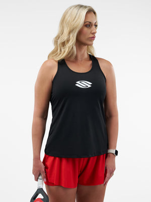 Blonde woman in black tank top with white logo and red shorts holding a paddle at her side, studio background