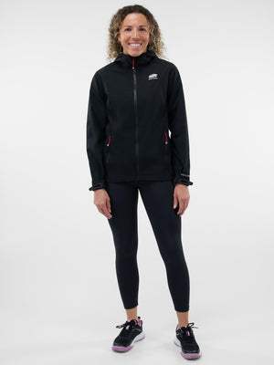 Smiling woman standing full-length in a black hooded zip jacket with logo, black leggings and black running shoes
