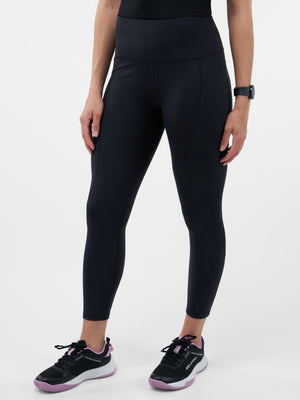 High-waist black ankle leggings with stitched panels, shown on a standing model and paired with black-and-pink running shoes.