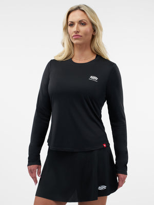 Woman model wearing black long-sleeve athletic top and matching black skort with small white brand logos on chest and hem.