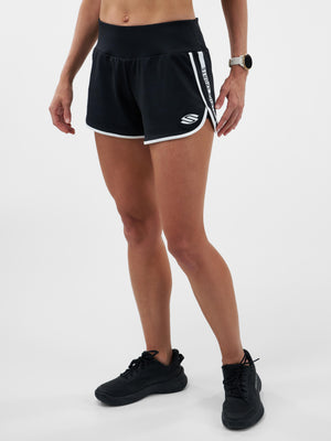 Woman wearing black athletic shorts with white trim and a vertical 'SPORTS' stripe, plus black sneakers