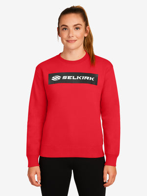 Model wearing red crewneck sweatshirt with black rectangular SELKIRK logo centered on chest