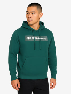 Male model wearing forest-green hoodie with kangaroo pocket and chest logo reading SELKIRK