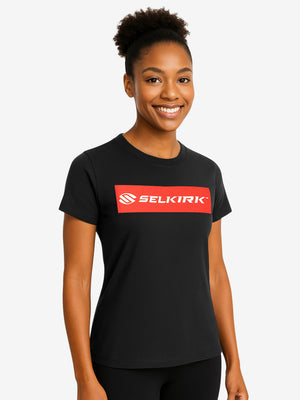 Smiling model wearing a black T-shirt with a red rectangular SELKIRK logo centered on the chest.