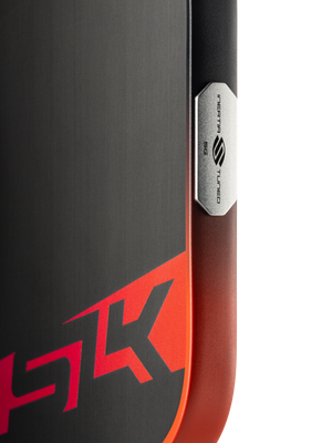 Close-up of SLK Dauntless pickleball paddle corner showing red SLK logo and metal INERTIA 5G TUNED badge on black-to-red gradient face