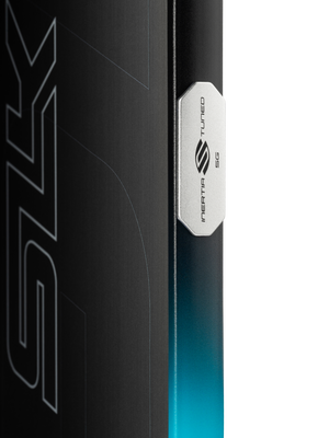 Close-up of SLK Geo pickleball paddle edge showcasing Inertia Tuned 5G metal badge and teal-to-black gradient finish on black background